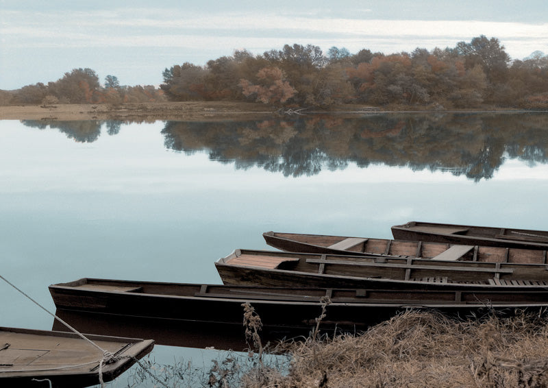 Wooden rowboats moored on a still river with autumn trees reflected in the water