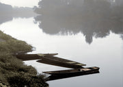 Three wooden boats moored on a still, foggy river with a misty tree-lined bank