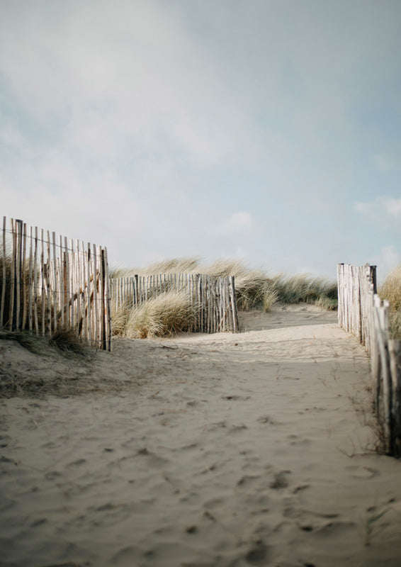 Sandy beach path flanked by wooden fences and dune grass under an overcast sky
