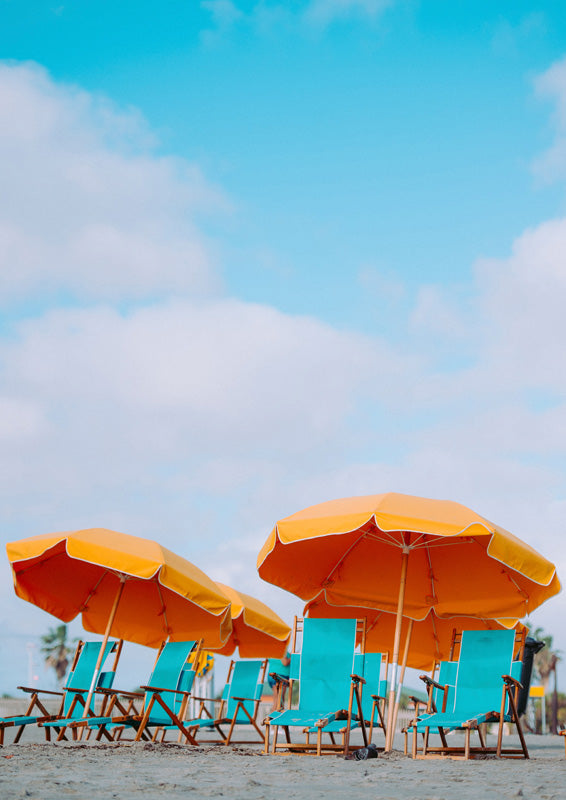 Orange beach umbrellas over teal chairs on sand under a blue sky