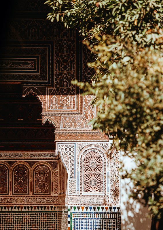 Carved Moroccan archway with ornate terracotta patterning beside blurred green tree foliage