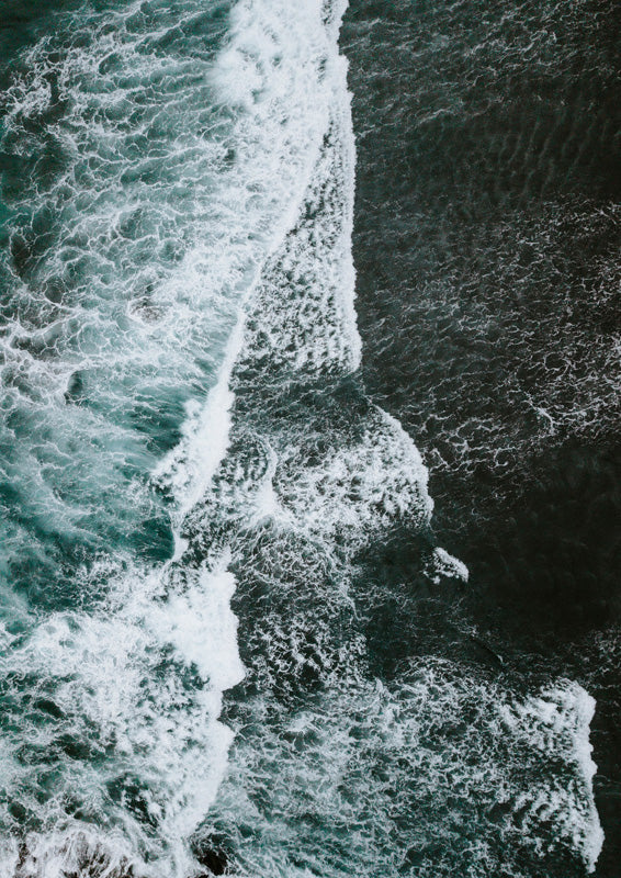 Aerial photo of ocean waves with white foam against deep teal and charcoal water