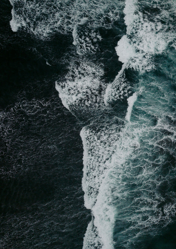 Aerial photograph of dark teal ocean water with white foam from breaking waves