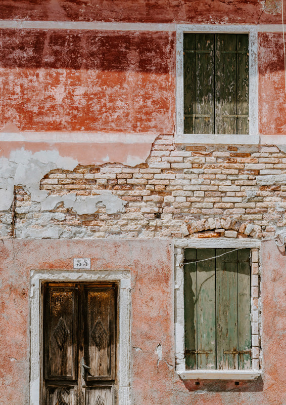 Weathered facade with terracotta render, exposed brick, green shutters and a numbered wooden door.
