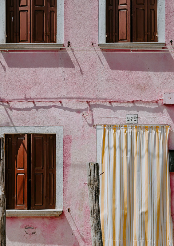 Weathered pink wall with brown shutters and a striped yellow curtain beside a numbered plaque