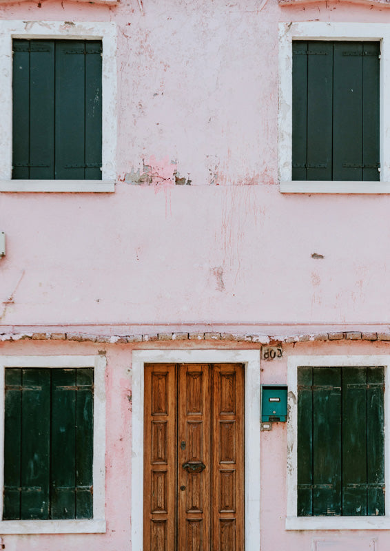Pink weathered building facade with green shutters and a wooden front door