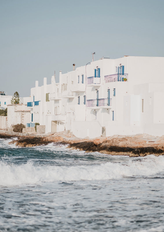 Whitewashed Mediterranean buildings above a rocky coast with waves breaking below