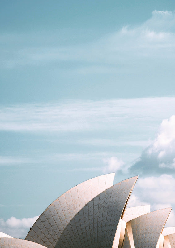 Close-up photograph of the Sydney Opera House sail roofs against a pale blue sky with soft clouds