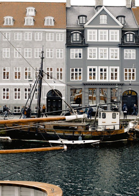 Grey and ochre gabled townhouses beside moored wooden boats on a European canal