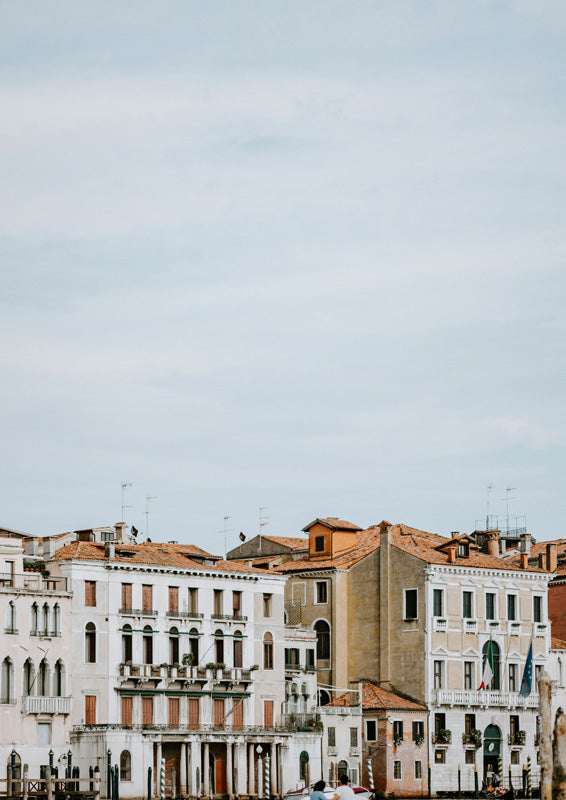 Row of Venetian buildings with terracotta roofs and pastel facades beneath a pale overcast sky