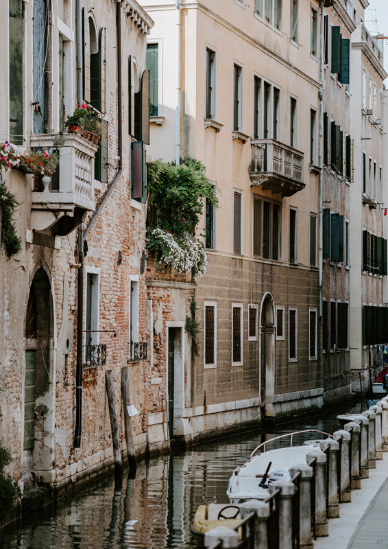 Venice canal lined with weathered buildings, balconies and flowers, with a moored boat in the foreground