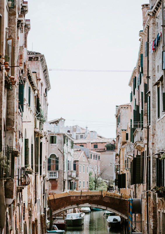 Photograph of a narrow Venice canal with weathered buildings, an arched bridge and moored boats