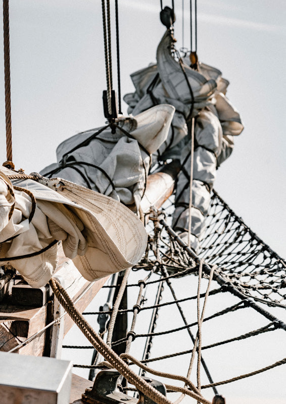 Bundled sailcloth and rope rigging on a tall ship against a pale sky