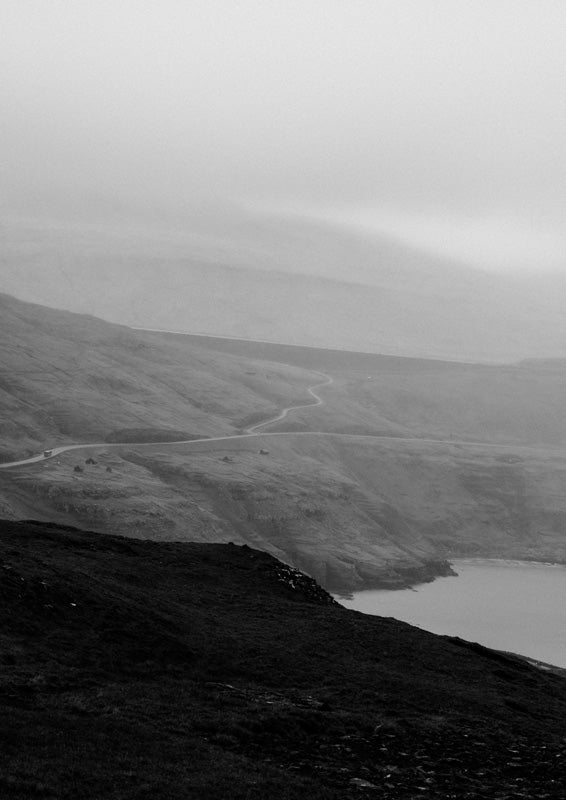 Black and white landscape photo of a winding road through misty hills above water
