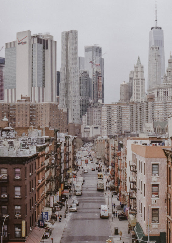 Aerial view of a New York City street lined with brick buildings, leading to a distant skyscraper skyline
