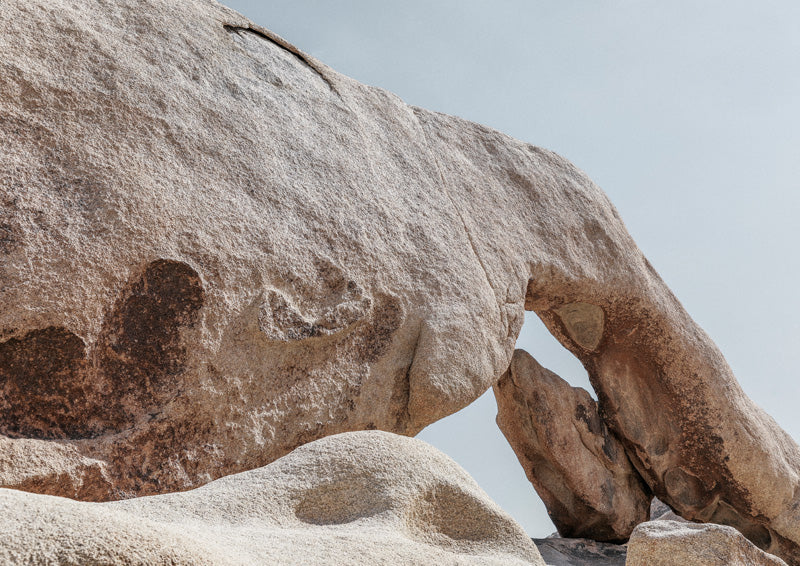 Close-up photograph of a sandstone boulder forming a natural arch against pale sky