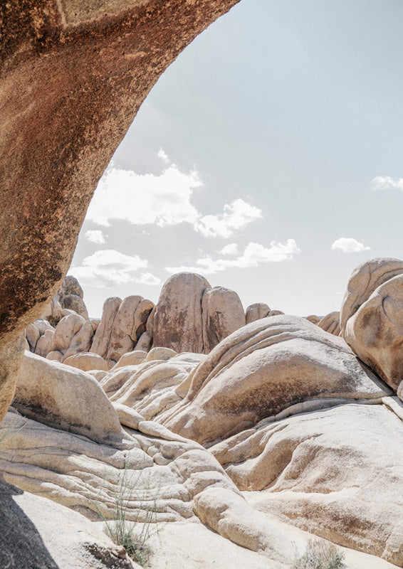 Rounded granite boulders and a rock overhang in a pale desert landscape under soft clouds