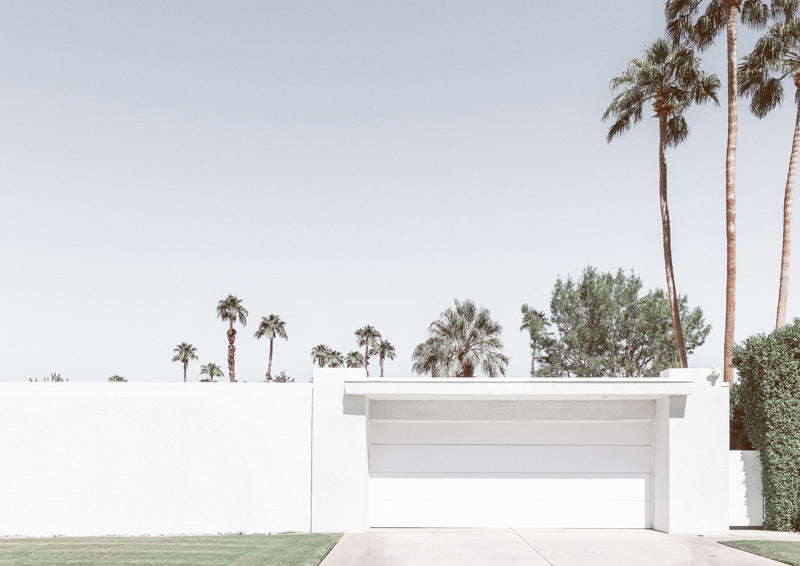 White mid-century home with flat-roofed carport and tall palm trees against pale sky