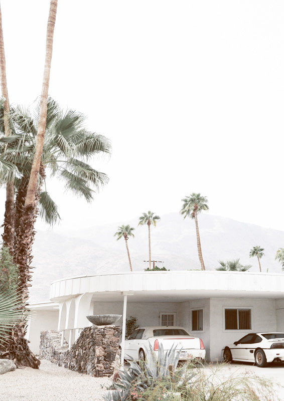 Curved white mid-century home with palm trees, mountains and parked white cars in Palm Springs
