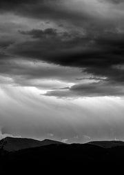 Black and white photo of sunbeams breaking through storm clouds over silhouetted hills