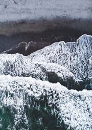 Aerial view of waves and white foam breaking on a dark sand beach