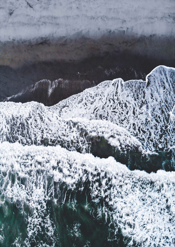 Aerial view of waves and white foam breaking on a dark sand beach