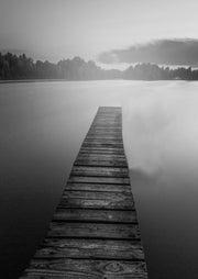 Black and white photo of a wooden jetty extending into calm water under an overcast sky
