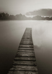 Sepia toned photograph of a wooden dock stretching across a misty lake toward distant trees