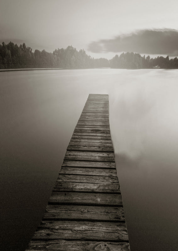 Sepia toned photograph of a wooden dock stretching across a misty lake toward distant trees