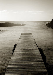 Sepia photograph of a wooden pier extending into calm ocean water between rocky outcrops
