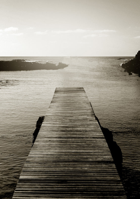 Sepia photograph of a wooden pier extending into calm ocean water between rocky outcrops