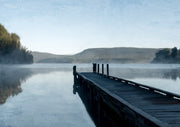Wooden dock extending into a misty lake with hills and trees in muted blue tones