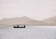 Silhouette of two fishermen in a small boat with mountains and pale sky behind