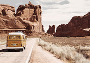 Yellow vintage campervan driving through a red rock desert canyon on a highway