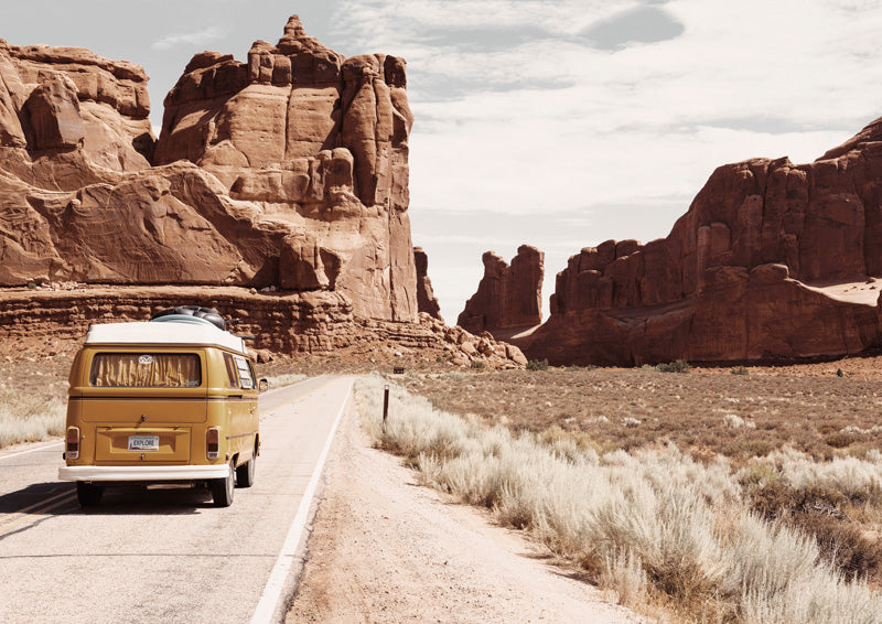 Yellow vintage campervan driving through a red rock desert canyon on a highway