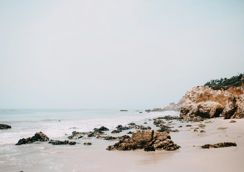 Pale sandy beach with rocks, calm ocean and a sandstone cliff under a hazy sky
