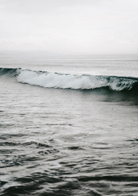 Black and white photograph of a breaking ocean wave under a pale sky