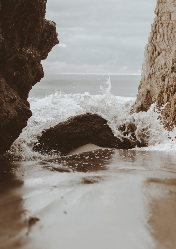 Waves crashing between rock formations onto wet sand in sepia and grey tones