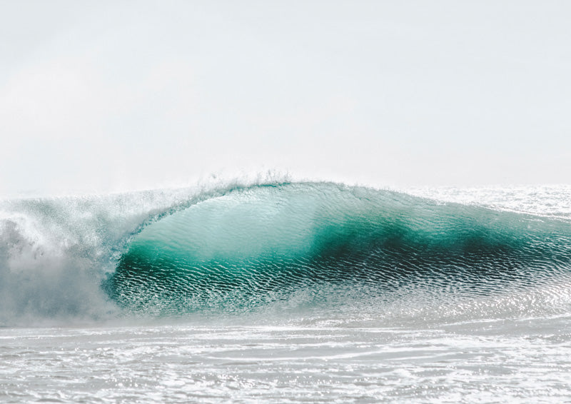 Close-up of a breaking teal ocean wave with white foam under a pale grey sky