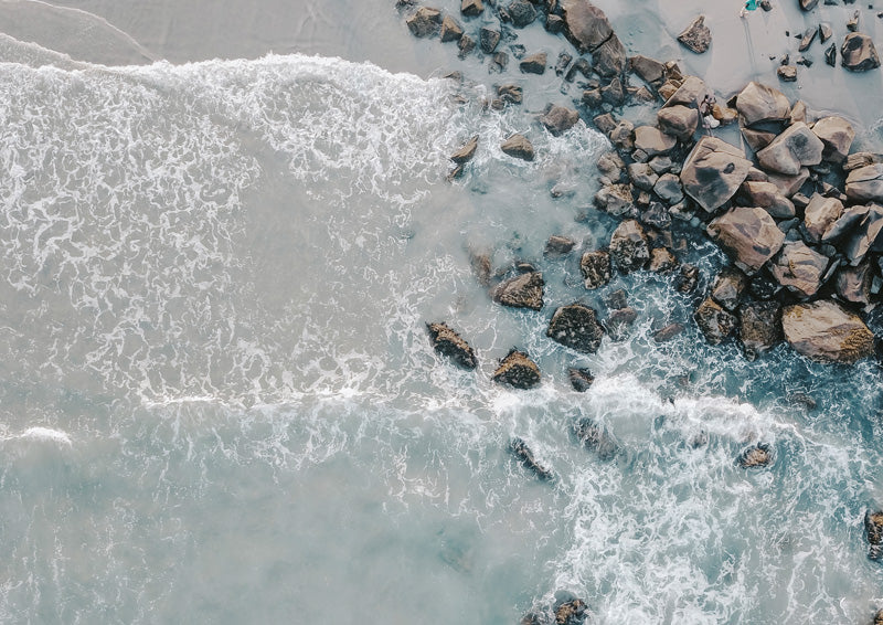 Aerial photo of ocean waves breaking against rocks on a beach