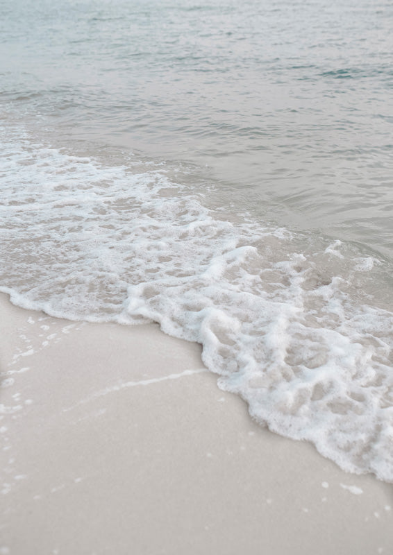 Close-up of a foamy wave washing over pale sand with soft grey-white tones