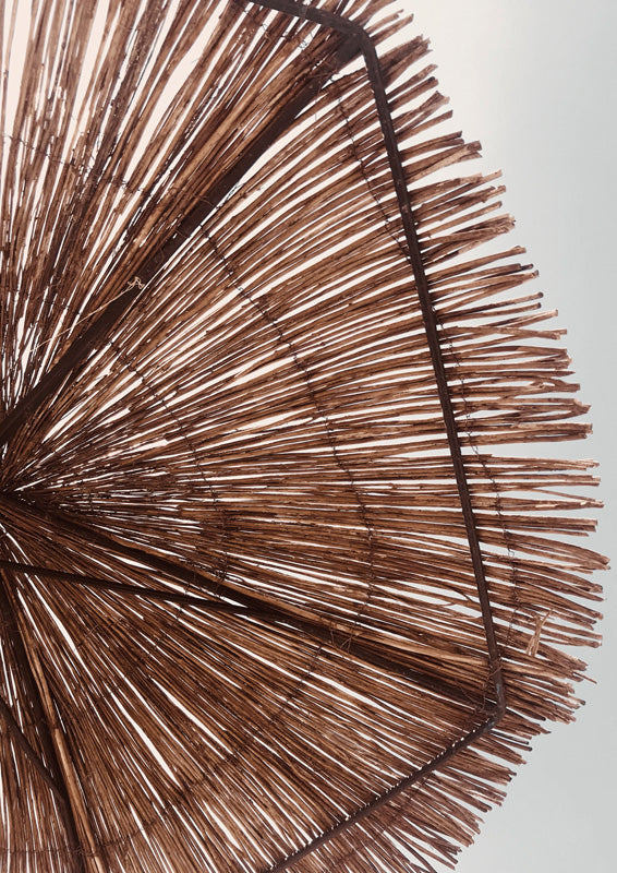 Close-up of a thatched straw umbrella with radiating brown fibers against a cream background
