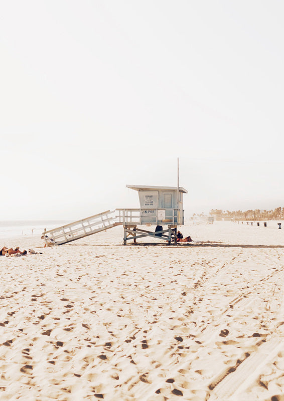 Lifeguard tower on a pale sandy beach with scattered beachgoers and distant palm trees