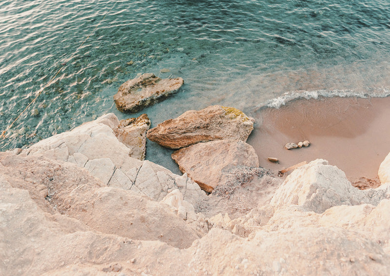 Aerial photograph of rocky coastline with teal water and sandy shore