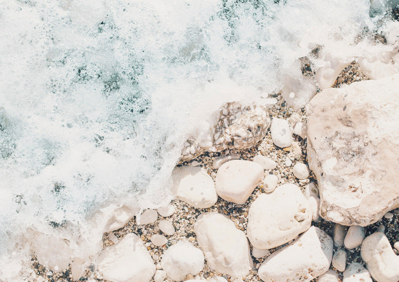 Aerial view of sea foam washing over pale rocks and pebbles on a beach