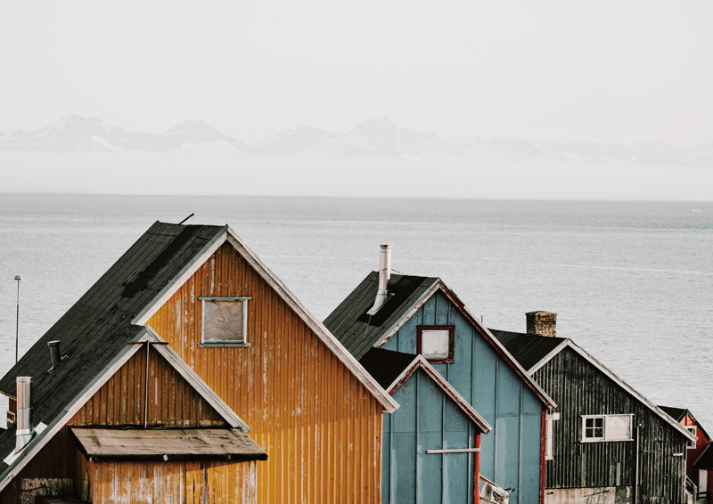 Weathered gabled houses in yellow, blue and charcoal beside water with misty mountains behind