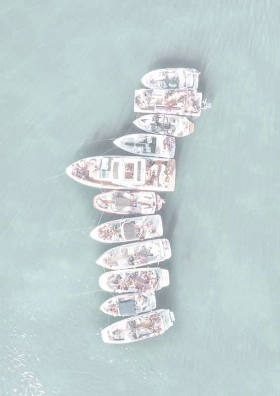 Aerial view of white boats tied together on pale teal water
