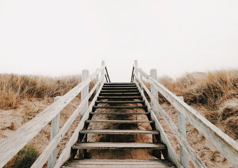 Wooden staircase rising through sandy dunes and grass under a pale overcast sky