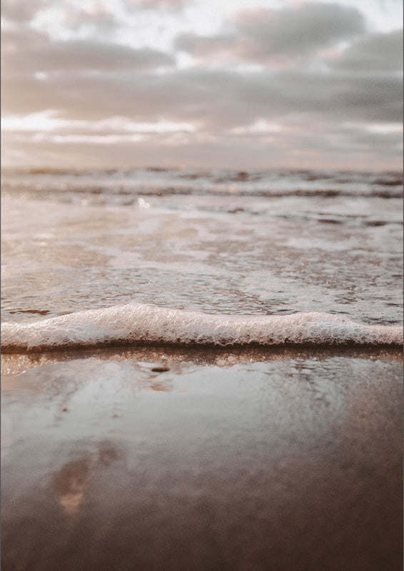 Low-angle photograph of sea foam on wet sand with a hazy, muted sky in the background