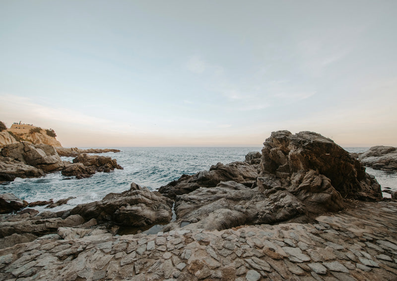 Rocky coastline at sunset with calm ocean and muted blue and peach sky tones